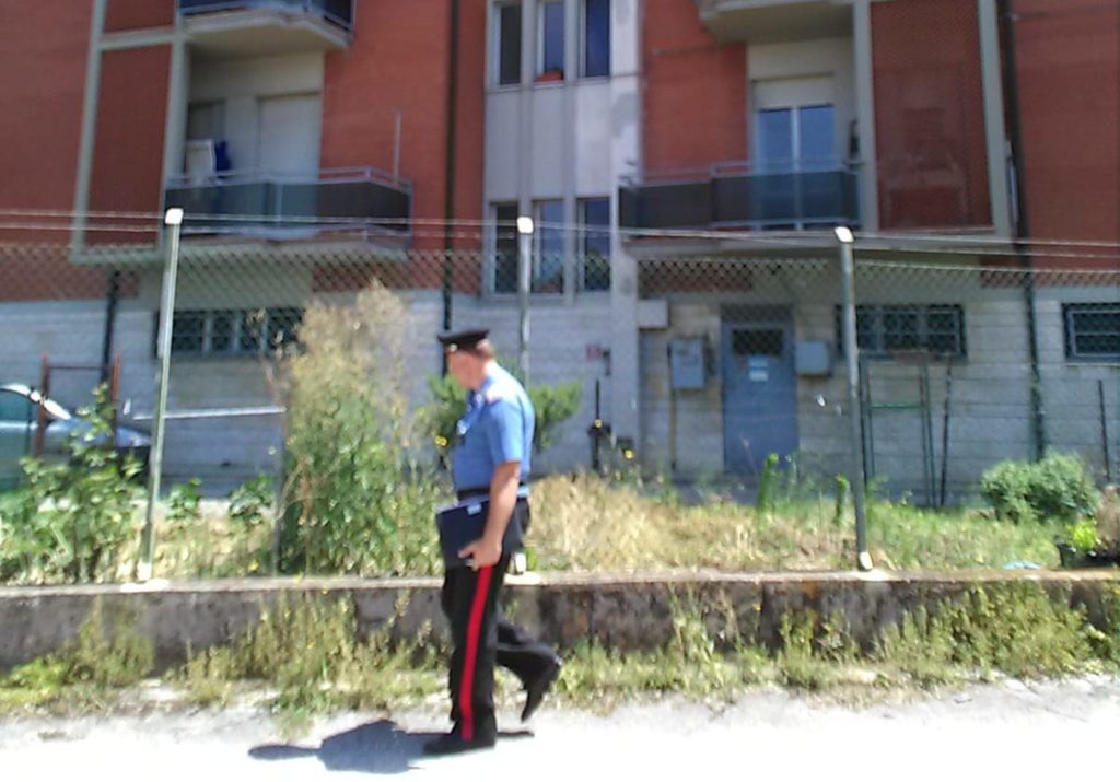 I carabinieri sul posto. Nello sfondo il palazzo dove è stata trovata senza vita la donna