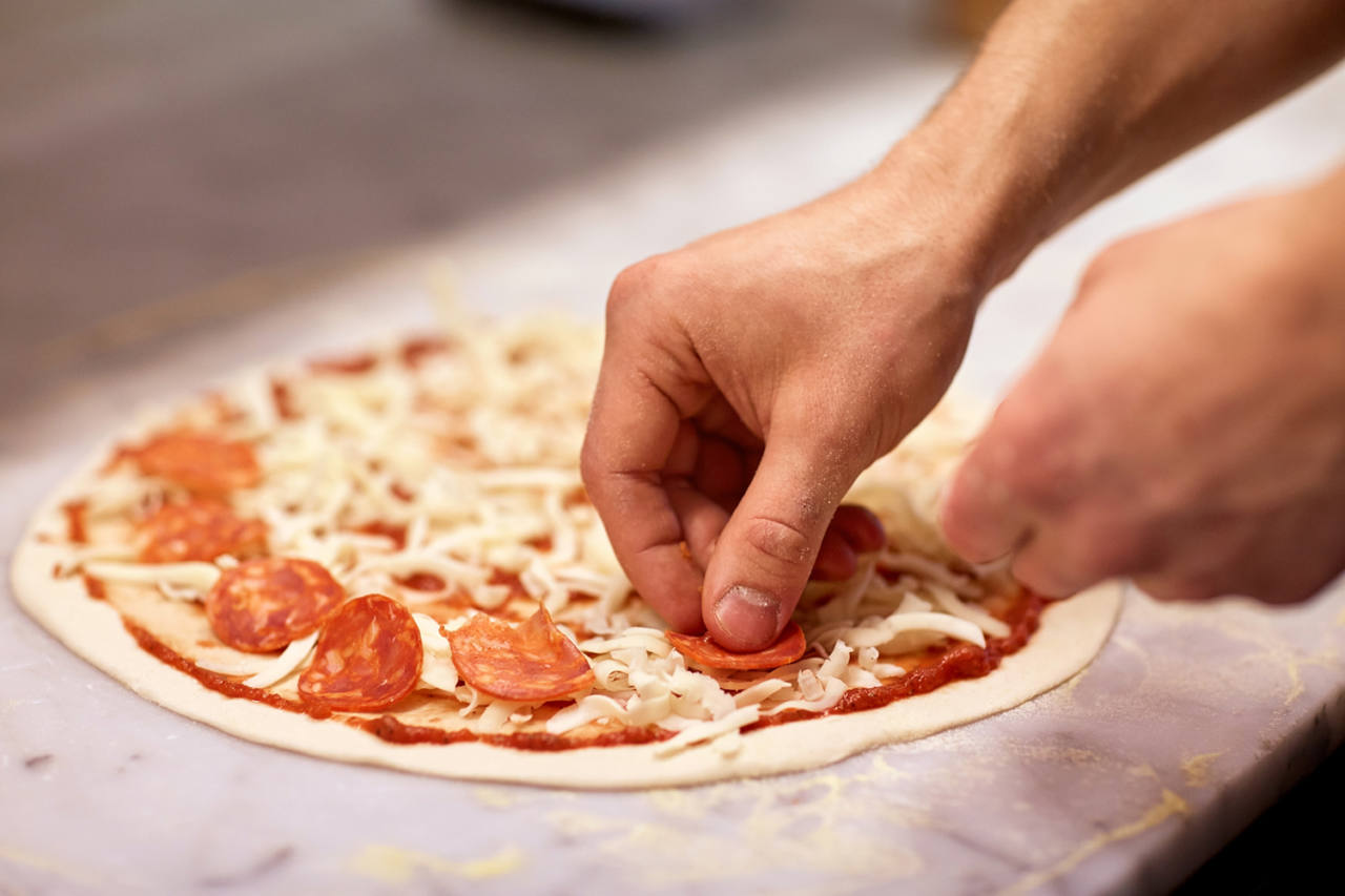 food, culinary, italian cuisine, people and cooking concept - cook hands adding salami slices to pizza at pizzeria