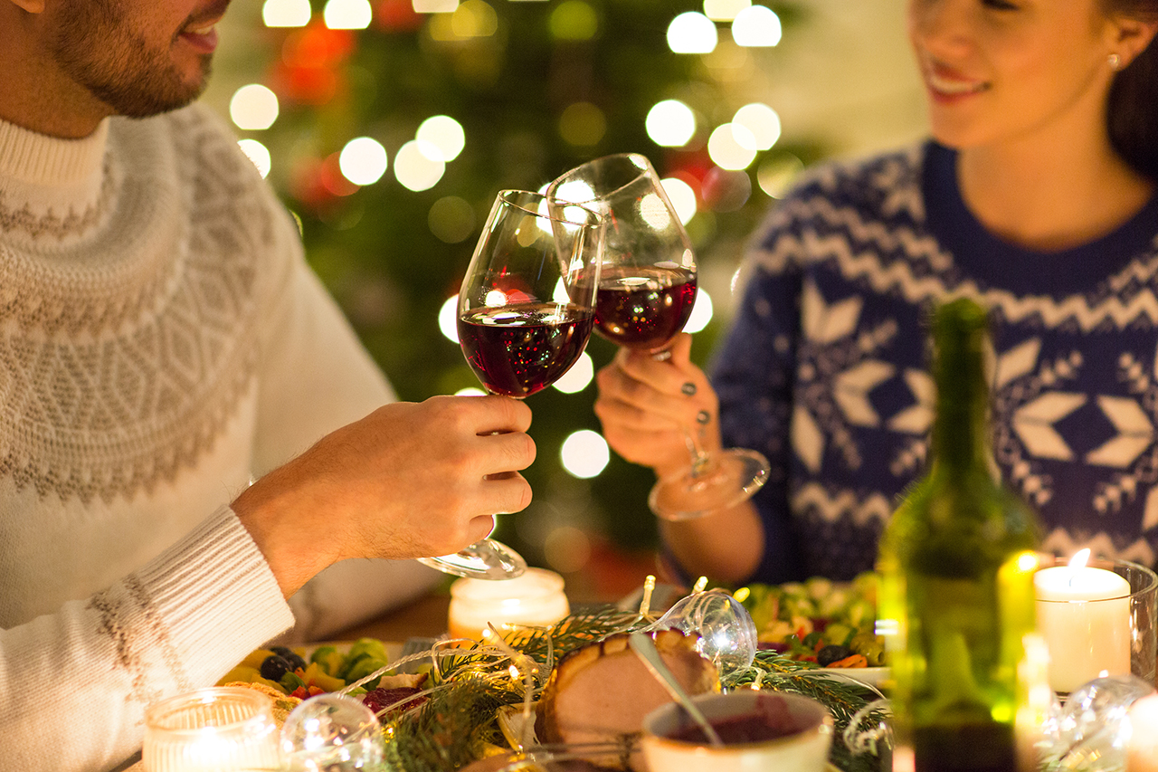 holidays, family and celebration concept - close up of happy couple having christmas dinner, drinking red wine and clinking glasses