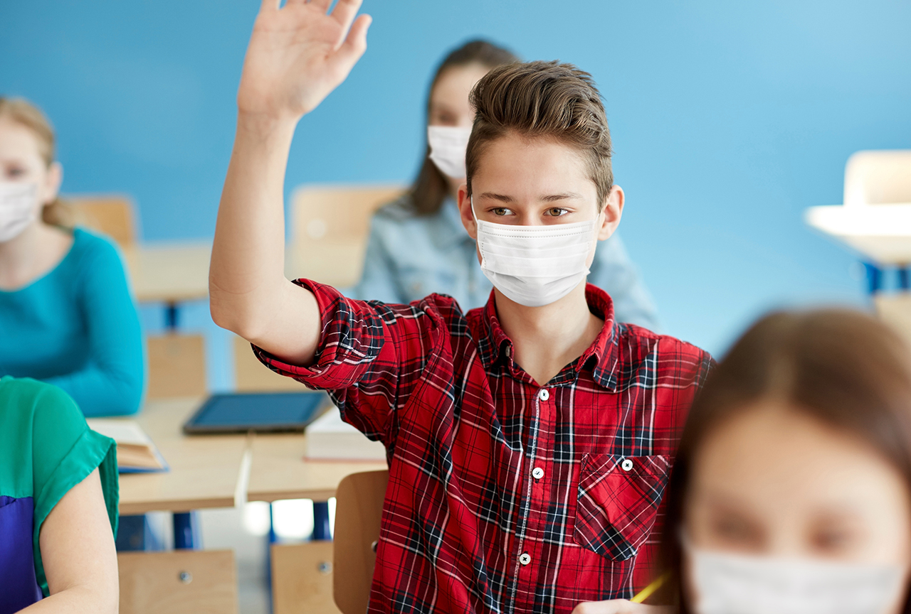 education, healthcare and pandemic concept - student boy wearing face protective medical mask for protection from virus disease with raised hand at school lesson